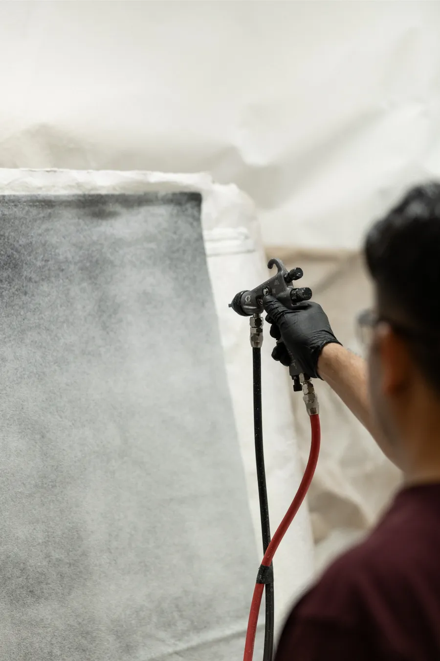 Technician spray-coating a part inside a paint booth