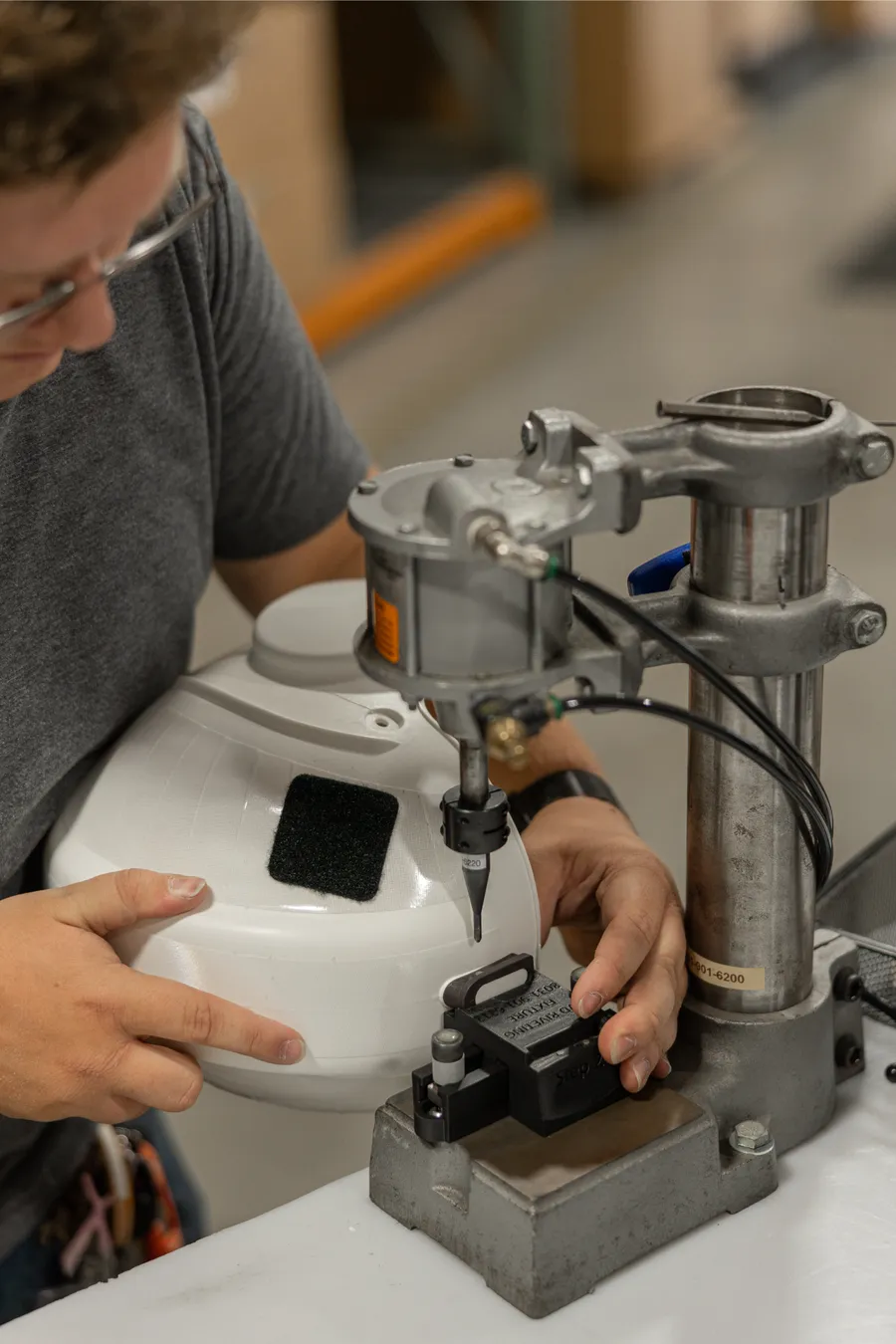 Technician positioning a white helmet shell in a bench press fixture